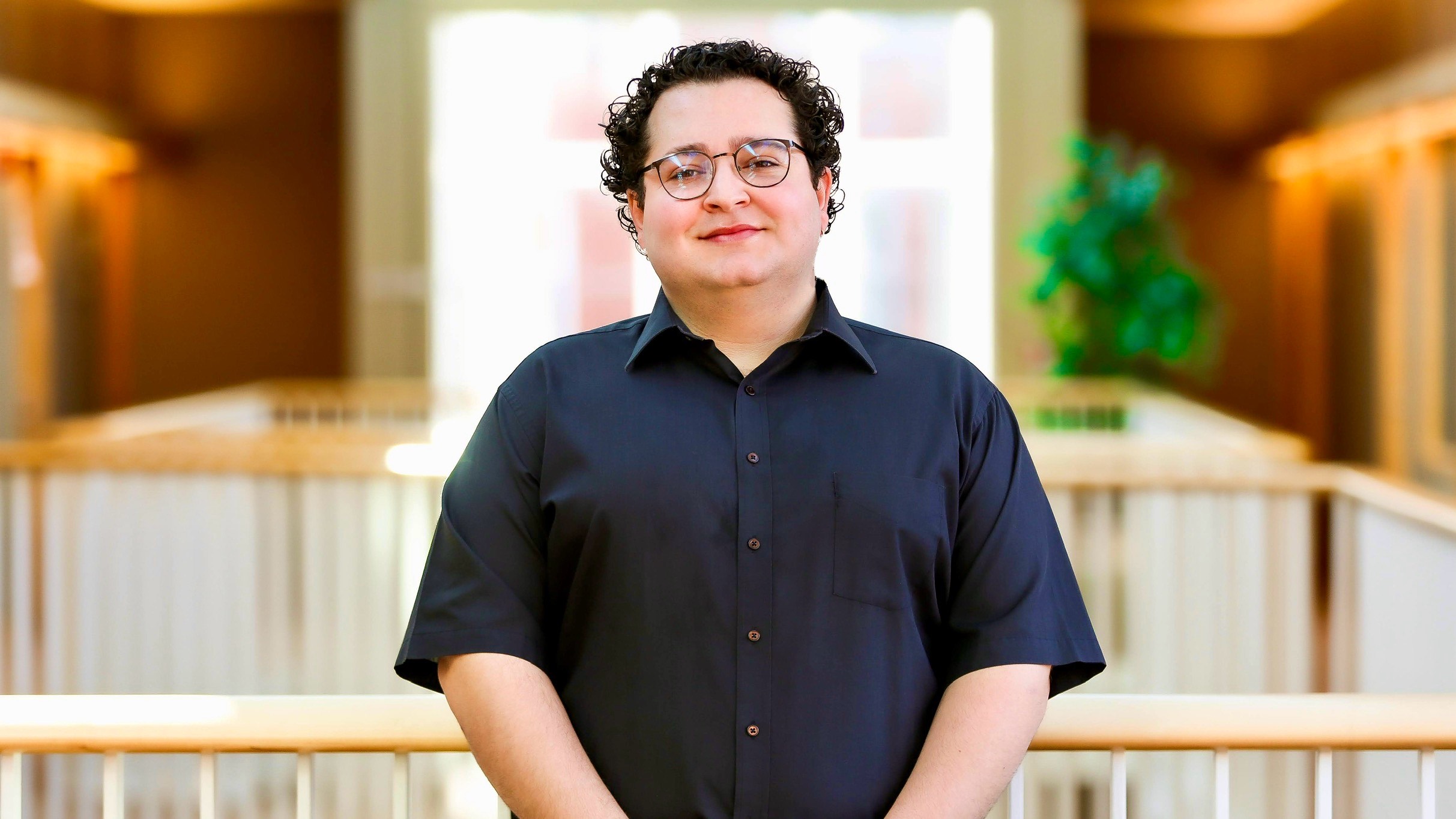 Person with curly hair and glasses smiling slightly looking straight ahead.