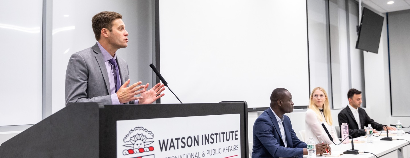 Dr. Adam Levine speaking at podium. Panelists seated to his right.