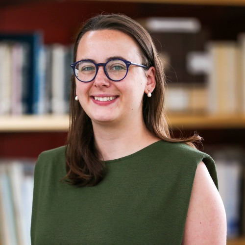 Image depicts Margaret Murphy in front of books, wearing green shirt and glasses.