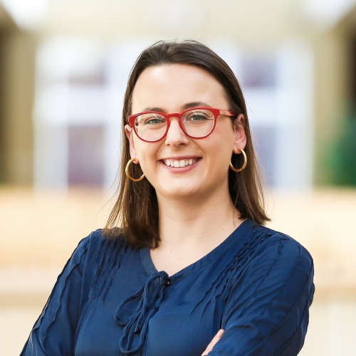 Woman with short brown hair and red glasses smiling. 