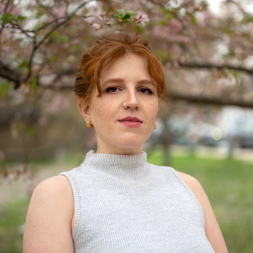Woman with red hair wearing grey top looking straight ahead.