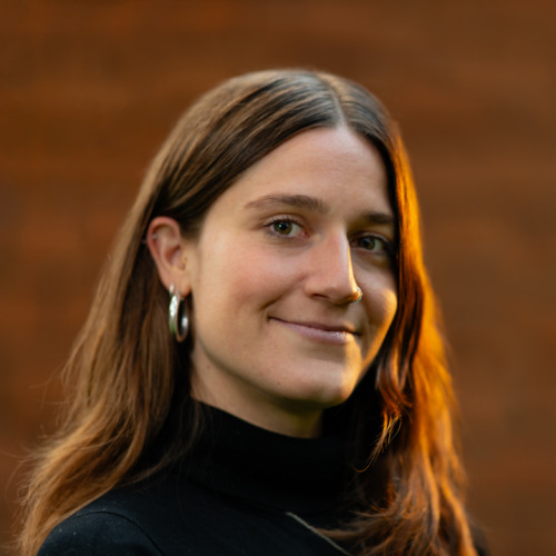Woman with long brown hair smiling. Wearing a black turtleneck and silver earrings. 
