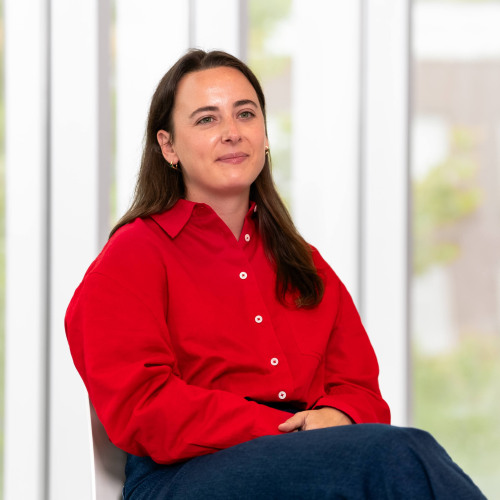Woman in red shirt with brown hair smiling softly. 