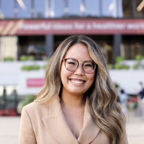 Woman with glasses wearing a tan blazer smiling. 