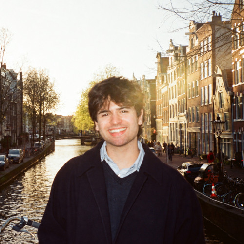 Brunette man standing in front of Amsterdam canals with sunshine in background