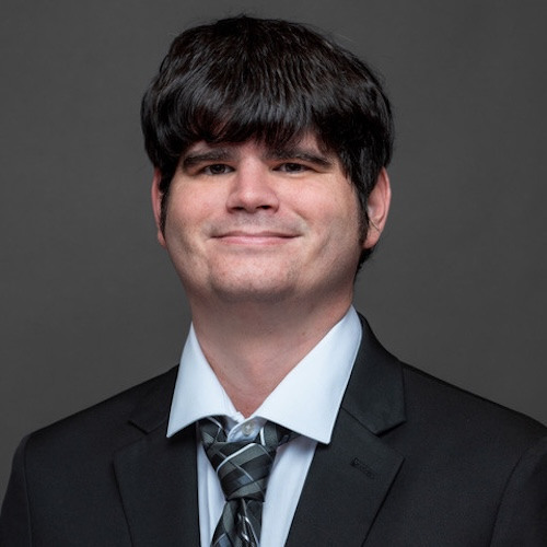 Man with black hair smiling with his mouth closed wearing a suit. 